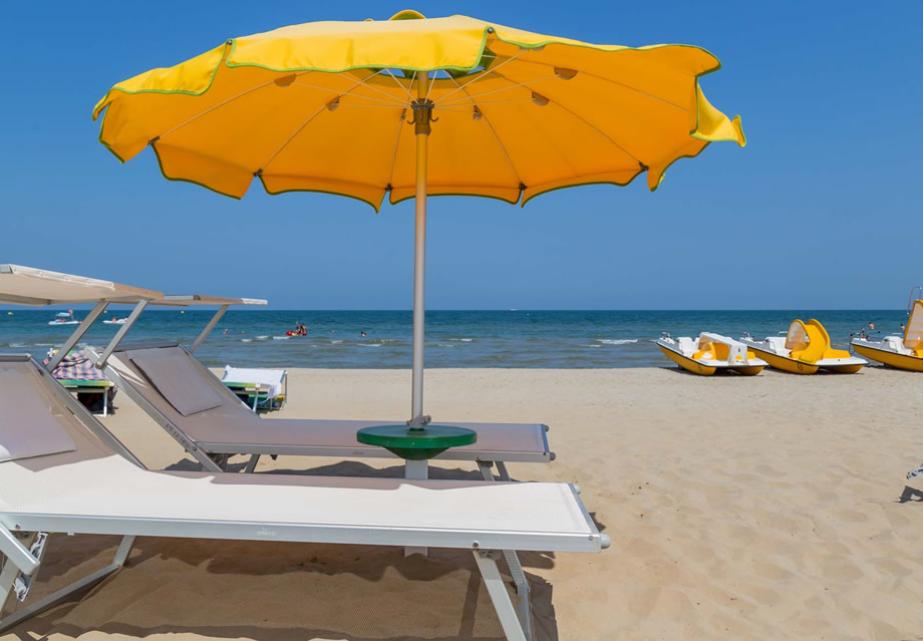 Spiaggia soleggiata con ombrellone giallo, sdraio e mare calmo, atmosfera rilassante.