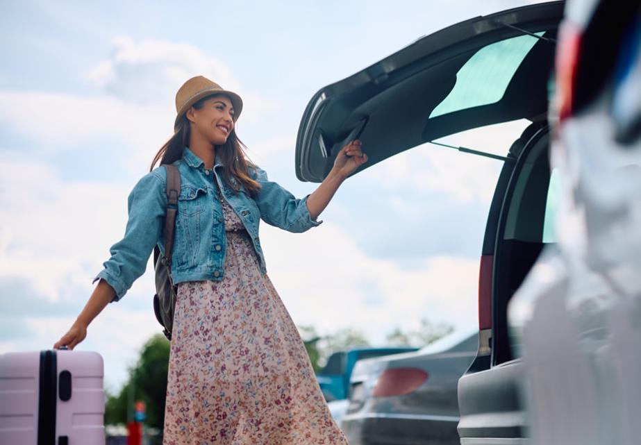 Donna sorridente con cappello carica bagagli in auto, atmosfera di viaggio e avventura.
